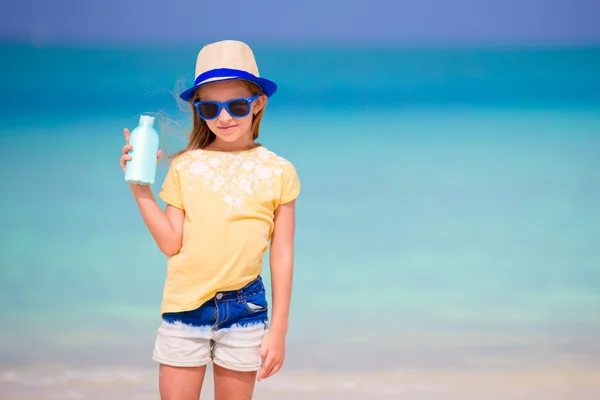 Little adorable girl with suntan lotion bottle on the beach