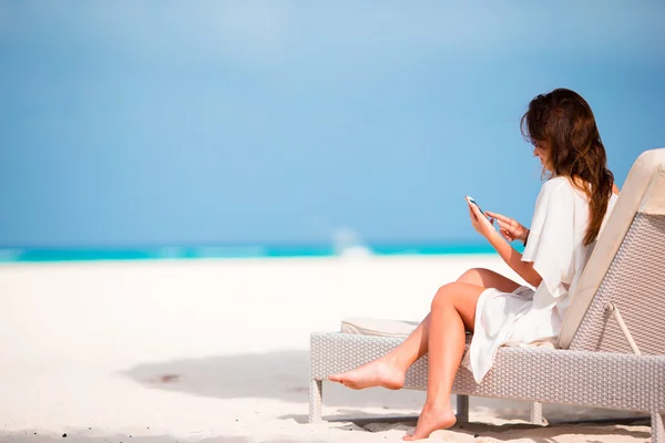 Jovem mulher na espreguiçadeira com telefone celular na praia — Fotografia de Stock