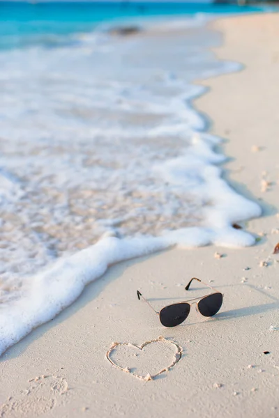 Closeup of sunglasses and heart on tropical beach — Stock Photo, Image