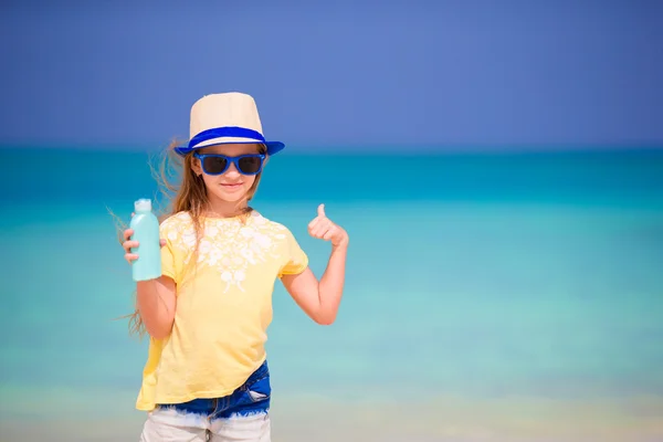 Niña adorable con botella de crema solar en la playa —  Fotos de Stock