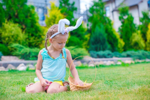 Adorable little girl wearing bunny ears holding basket with Easter eggs — Stock Photo, Image