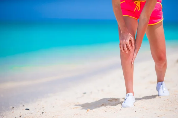 Atleta femenina que sufre de dolor en la pierna mientras hace ejercicio en la playa blanca —  Fotos de Stock