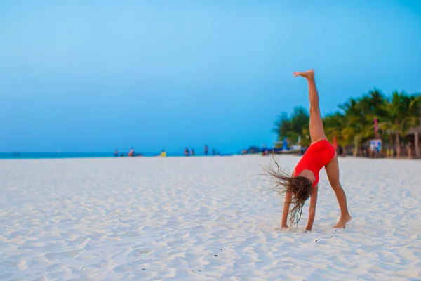 Entzückendes kleines Mädchen, das Spaß beim Wagenradmachen am tropischen Strand bei Sonnenuntergang hat — Stockfoto