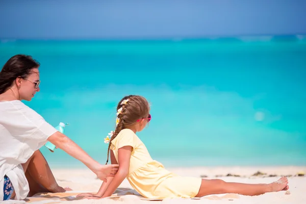 Мать наносит солнцезащитный крем своей дочери на тропический пляж — стоковое фото