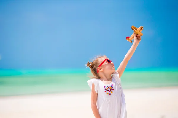 Adorable little girl with toy airplane in hands on white tropical beach — Stock Photo, Image