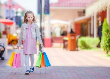 Büyük alışveriş merkezinde alışveriş torbaları ile sevimli gülümseyen küçük kız