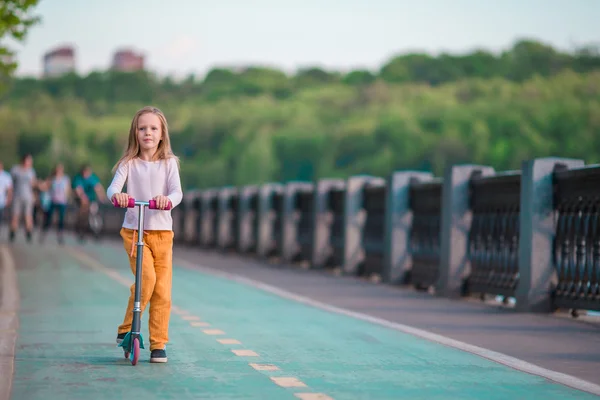 Adorable little girl riding her scooter in a summer park — Stock Photo, Image