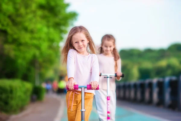 Little adorable girls riding on scooters in park outdoors — Stock Photo, Image