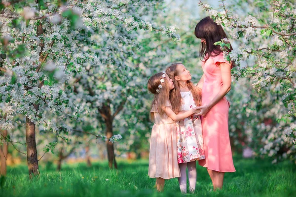 Adorables petites filles avec jeune mère dans le jardin de cerises en fleurs sur la belle journée de printemps — Photo