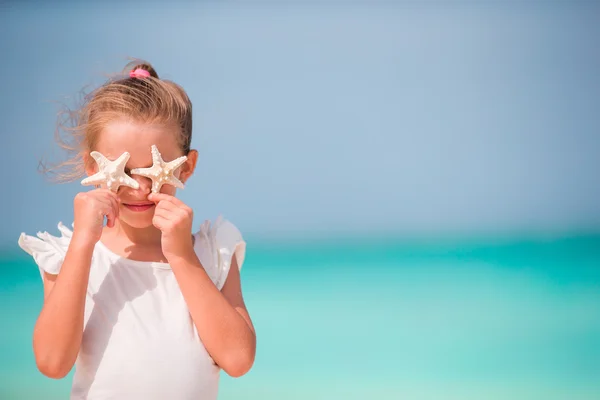 Entzückendes kleines Mädchen mit Seesternen am Strand — Stockfoto