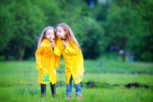 Funny cute toddler girls wearing waterproof coat playing outdoors by rainy and sunny day — Stock Photo, Image