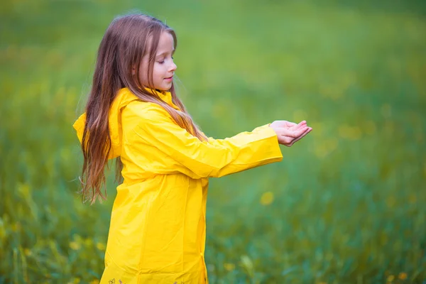 Adorable niña pequeña con abrigo impermeable jugando al aire libre por el día lluvioso y soleado — Foto de Stock
