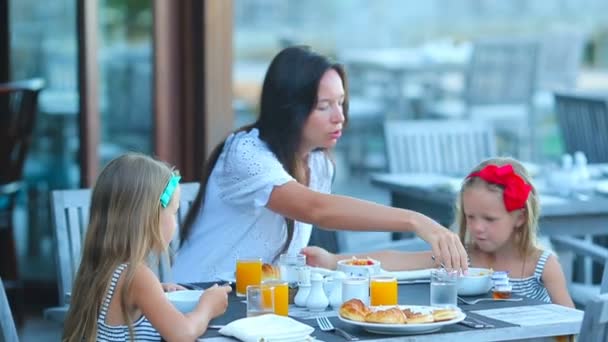 Jeune mère et adorables petites filles prenant le petit déjeuner au café extérieur — Video