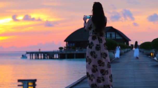 Mujer joven tomando fotos de la hermosa puesta de sol en vacaciones tropicales — Vídeos de Stock