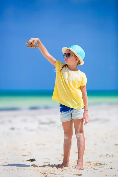 Gelukkig klein meisje met speelgoed vliegtuig in handen op wit zandstrand — Stockfoto