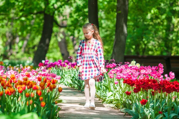 Liten bedårande flicka i blommande tulpaner trädgård. Varm vårdag utomhus — Stockfoto