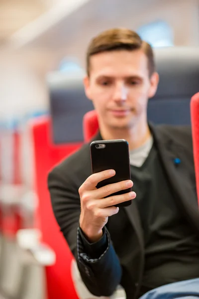 Giovane uomo felice che viaggia in treno. Turista scrivere un messaggio sul cellulare durante il viaggio in treno espresso — Foto Stock