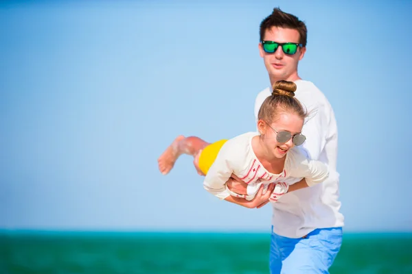 Happy father and his adorable little daughter at tropical beach. Caucasian family having fun together on suumer vacation on white beach running and enjoying their holidays — Stock Photo, Image