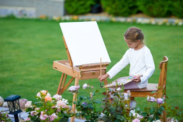 Bedårande liten flicka måla en bild på staffli utomhus. Lite konstnär förtjust i hennes hobby. — Stockfoto