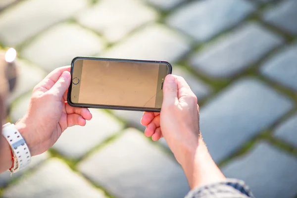 Fecho do celular em mãos masculinas fundo da rua. Homem usando smartphone móvel . — Fotografia de Stock