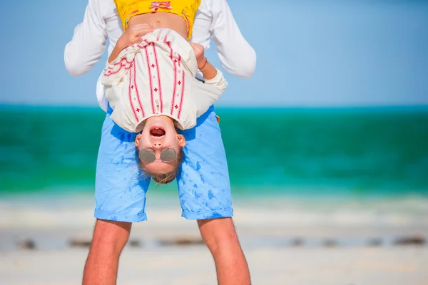 Счастливый отец и его очаровательная маленькая дочь на тропическом пляже веселятся. Ребенок висит вверх ногами в руках ее отца — стоковое фото