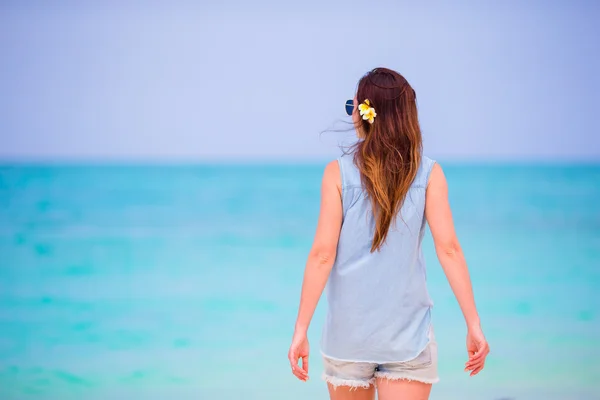 Joven hermosa mujer durante las vacaciones en la playa tropical. Disfrute de vacaciones suumer solo en la playa de África con flores de frangipani en su cabello — Foto de Stock