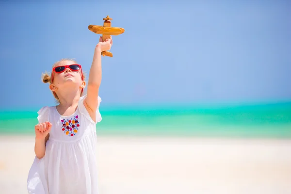 Gelukkig klein meisje met speelgoed vliegtuig in handen op witte zandstrand. Foto reizen reclame, vluchten en luchtvaartmaatschappijen — Stockfoto