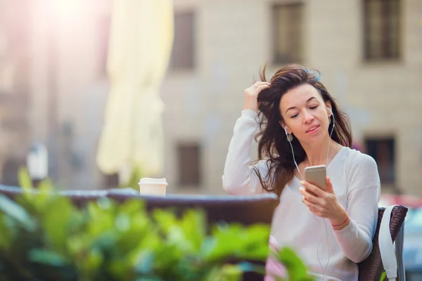 Jeune femme caucasienne envoyer un message et écouter de la musique dans un café en plein air — Photo