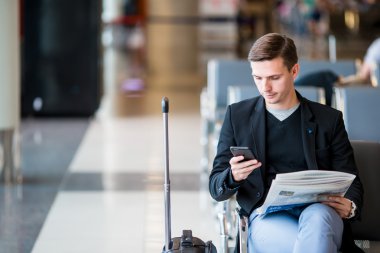 Havaalanı lobisindeki yolcu uçuş uçağını bekliyor. Havaalanında cep telefonu olan genç bir adam inişi bekliyor.