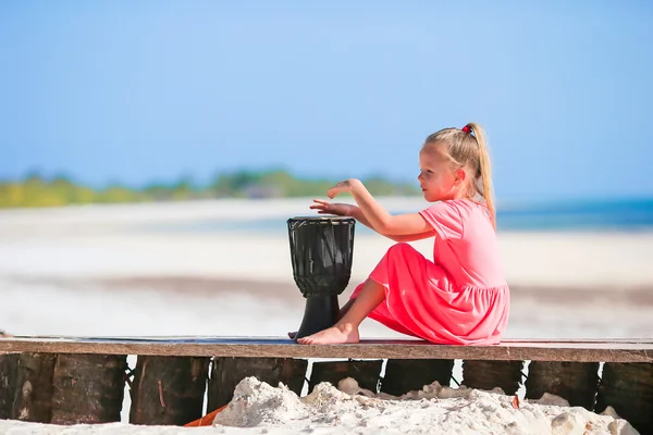 Kleines fröhliches Mädchen, das auf afrikanischen Trommeln spielt. entzückendes Kind hat Spaß mit afrikanischen Trommeln am weißen Strand — Stockfoto