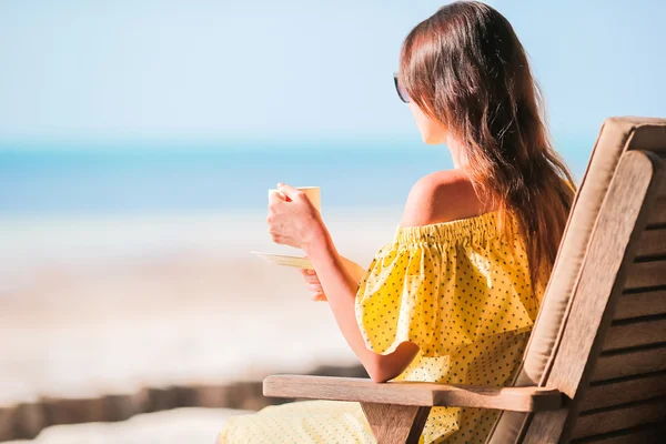 Mujer joven bebiendo café caliente disfrutando de vistas a la playa. Hermosa mujer relajarse durante vacaciones exóticas en la playa disfrutando de café dulce — Foto de Stock