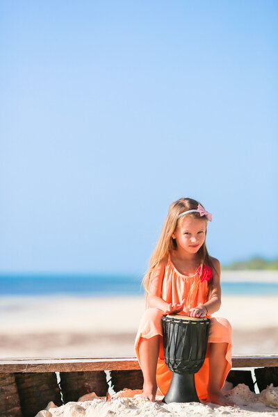 Little happy girl playing african drums. Adorable kid having fun with national african drums on white beach