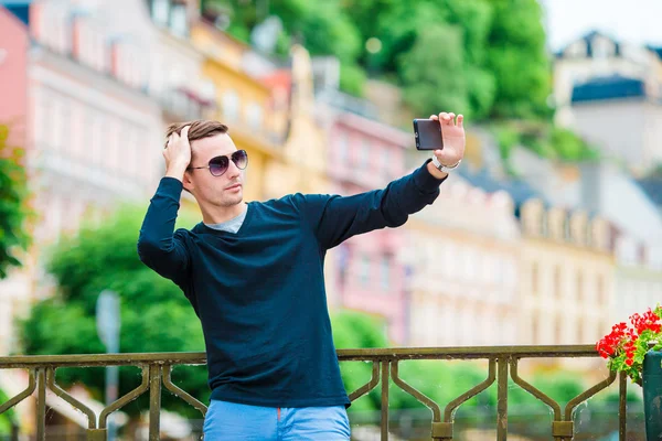 Homem turístico tirar fotos de viagem com smartphone em férias de verão. Jovem turista atraente tirar foto selfie com telefone celular ao ar livre desfrutando de férias destino de viagem no turismo e — Fotografia de Stock