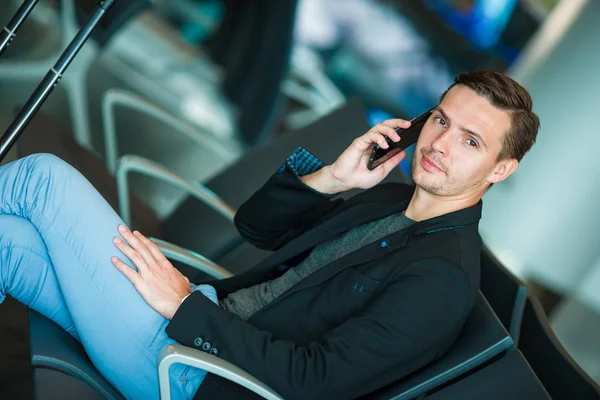 Hombre de negocios urbano hablando por teléfono inteligente viajando dentro en el aeropuerto. Joven hombre de negocios casual con chaqueta de traje. Modelo masculino guapo. Joven con celular en el aeropuerto mientras espera — Foto de Stock