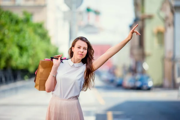 Jeune fille heureuse avec des sacs à provisions attraper un taxi. Portrait d'une belle femme heureuse debout dans la rue tenant des sacs à provisions souriant et attrapant un taxi — Photo