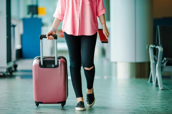 Pasajero de avión de primer plano con pasaportes y tarjeta de embarque y equipaje rosa en un salón del aeropuerto. Mujer joven en el aeropuerto internacional caminando con su equipaje . —  Fotos de Stock