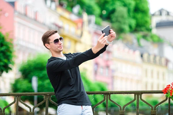 Homem turístico tirar fotos de viagem com smartphone em férias de verão. Jovem turista atraente tirar foto selfie com telefone celular ao ar livre desfrutando férias destino de viagem no turismo . — Fotografia de Stock
