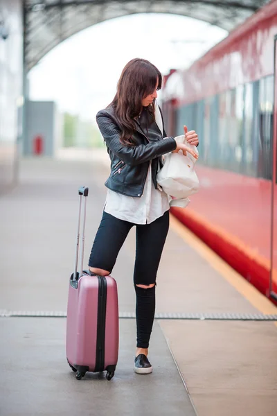 Mujer joven con equipaje hablando por celular en una estación de tren. Caucasiam turista esperando su expreso tren mientras su viaje . —  Fotos de Stock