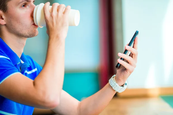 Gros plan de mains masculines tenant un téléphone portable et un verre de café dans un café. Homme utilisant un smartphone mobile. Garçon touchant un écran de son intelligence. Fond flou, horizontal . — Photo