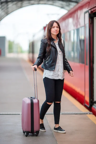 Молодая женщина с багажом разговаривает на вокзале. Caucasiam турист ждет ее экспресс-поезд в то время как ее отпуск — стоковое фото