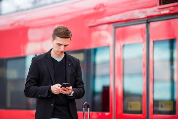 Ung kaukasisk man med smarttelefon och bagage på stationen reser med tåg — Stockfoto