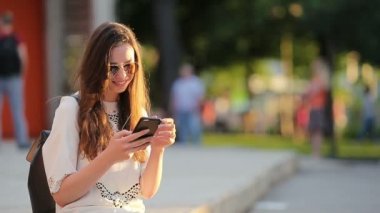 Beyaz bir kadın mesaj gönderiyor ve Avrupa 'da açık havada müzik dinliyor. Güneş gözlüklü güzel kız ahşap bankta akıllı telefon kullanarak oturuyor.