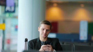 Akıllı telefon içinde havaalanında seyahat üzerinde konuşan kentsel iş adam. Casual genç işadamı giyen takım elbise ceketi. Yakışıklı erkek modeli. Genç adam için beklenirken havaalanında cep telefonu ile