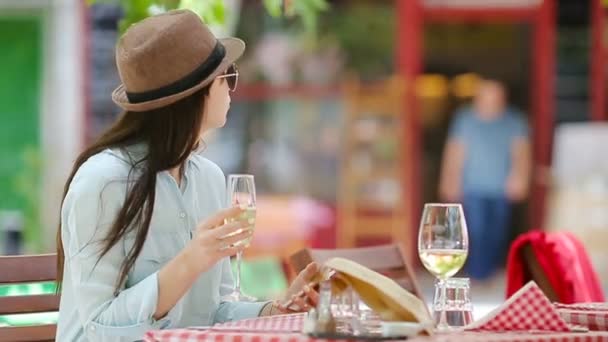 Chica joven con copa de vino blanco utilizando el teléfono inteligente en el café al aire libre. Hermosa mujer después de caminar sentado en la cafetería al aire libre con café y el uso de teléfono inteligente — Vídeos de Stock