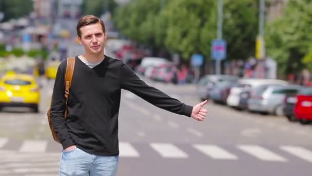 Junger glücklicher Mann nimmt in europäischen Straßen ein Taxi. Porträt eines kaukasischen Touristen mit einem lächelnden Rucksack und einem Taxi — Stockvideo