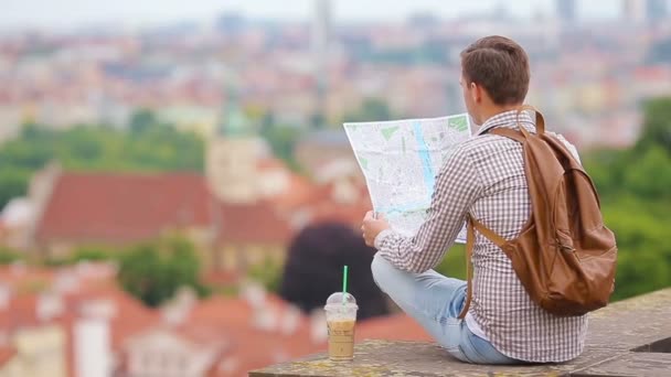 Mladý muž se město mapa a batoh pozadí Evropské město. Kavkazská turista při pohledu na mapu Evropského města s krásným výhledem atrakce. — Stock video