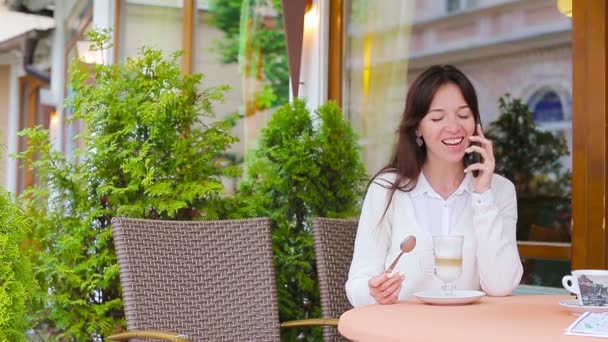 Retrato de mulher bonita sentada no café ao ar livre bebendo café e usando smartphone. Menina olhando instagram e beber delicioso cappuccino doce . — Vídeo de Stock