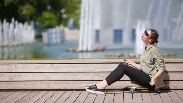 Mladá krásná dívka poslouchá hudbu a užijte si víkend na dřevěném mostě. Krásná hipster žena se sluchátky pomocí chytrého telefonu venku. — Stock video