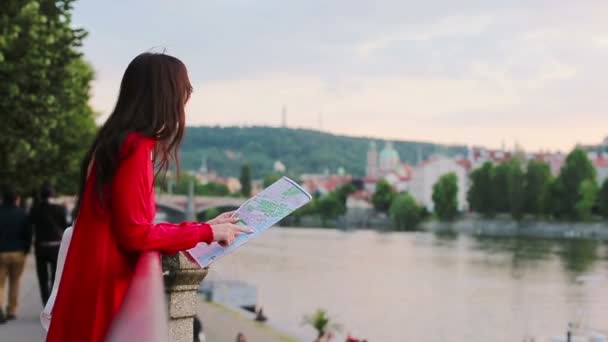 Счастливая молодая женщина с картой города на фоне знаменитого моста в Европе. Туристическая женщина с картой на улице во время отдыха в Европе . — стоковое видео