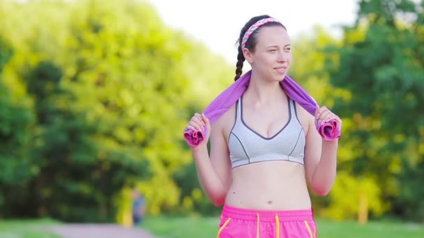 Beautiful young sport woman with towel. Portrait young attractive smiling fit woman with white towel resting after workout sport exercises outdoors on a background of park trees. Healthy lifestyle — Stock Video